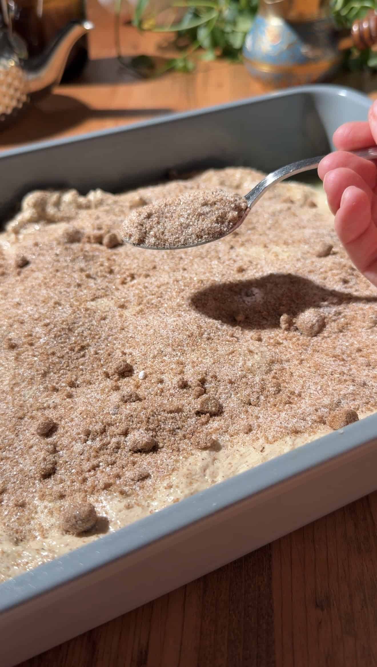 A hand sprinkling cinnamon sugar from a metal spoon onto focaccia dough in a baking dish.
