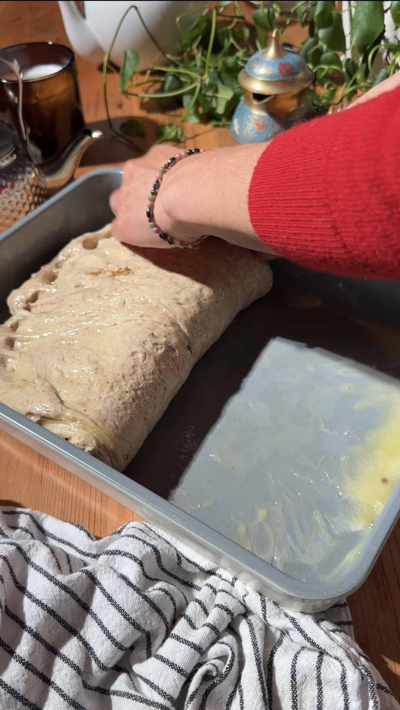 Two hands folding focaccia dough in half in a greased metal baking dish.