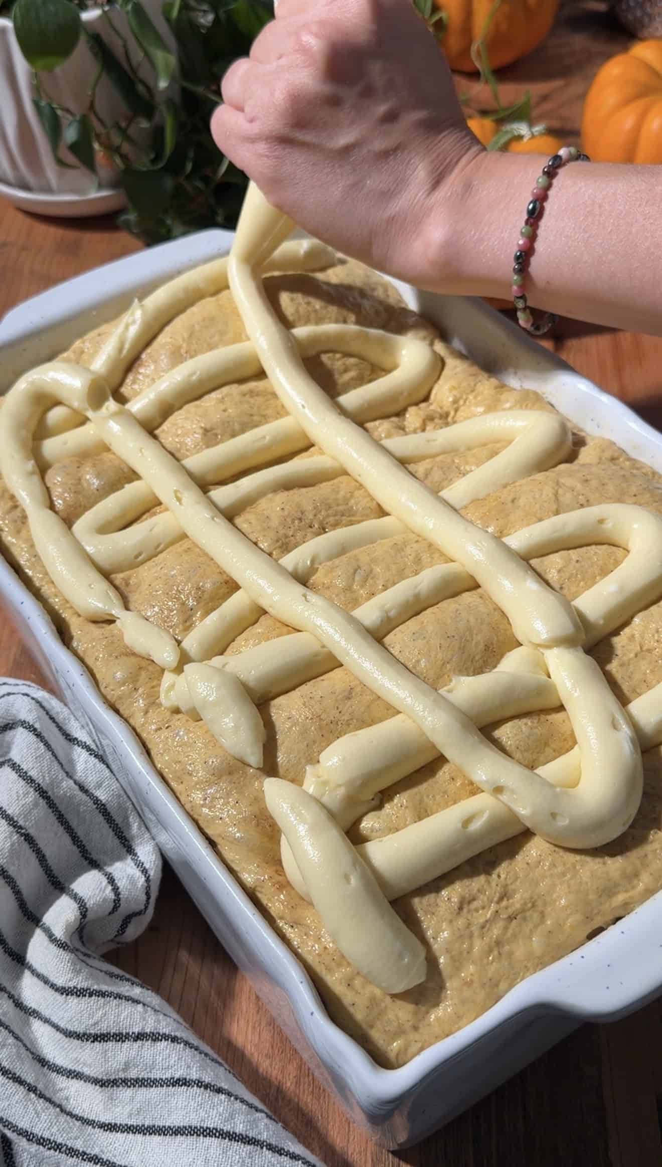 A hand piping cheesecake filling on top of puffy orange pumpkin focaccia dough.