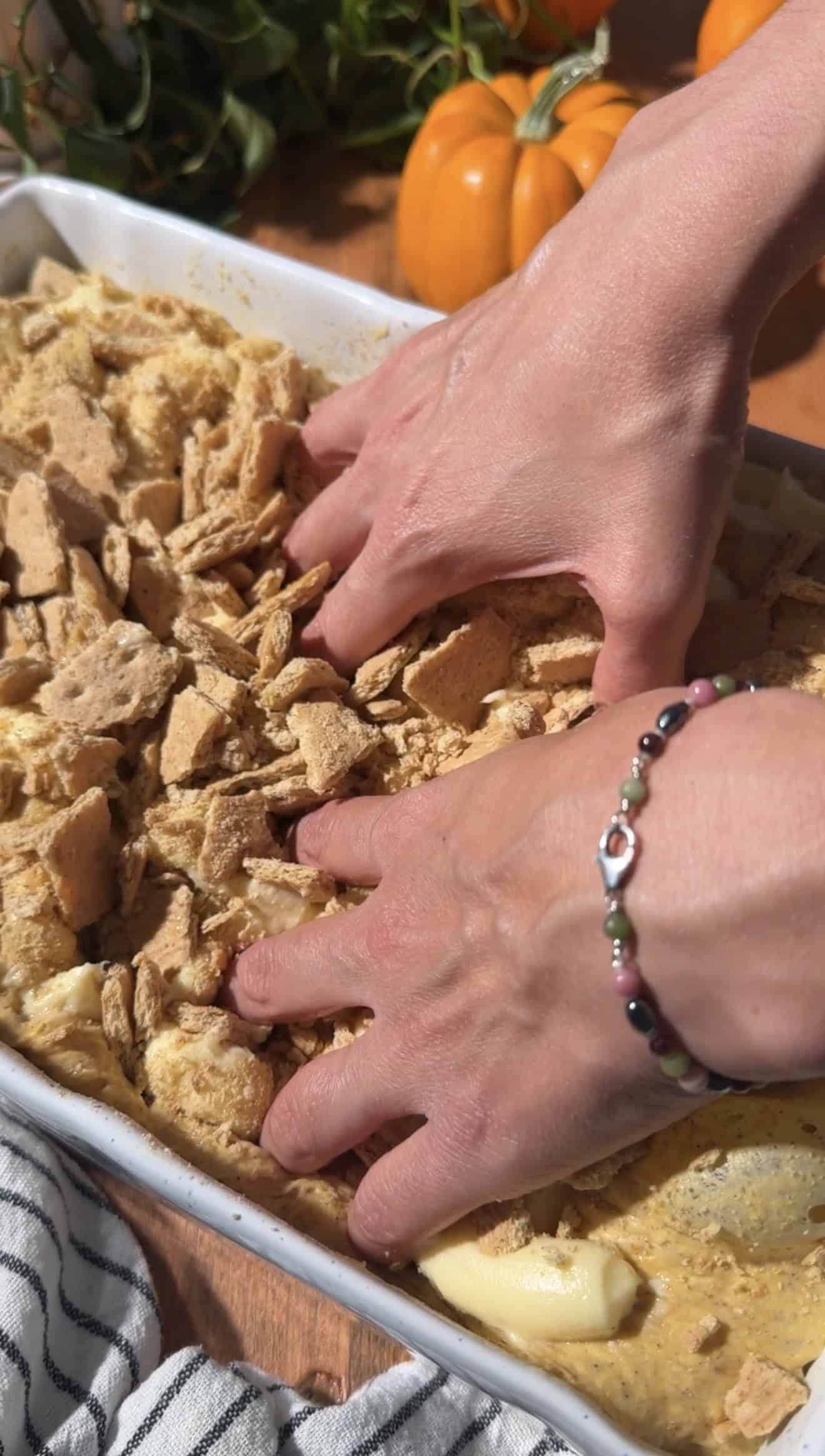 Two hands dimpling focaccia dough topped with graham crackers.