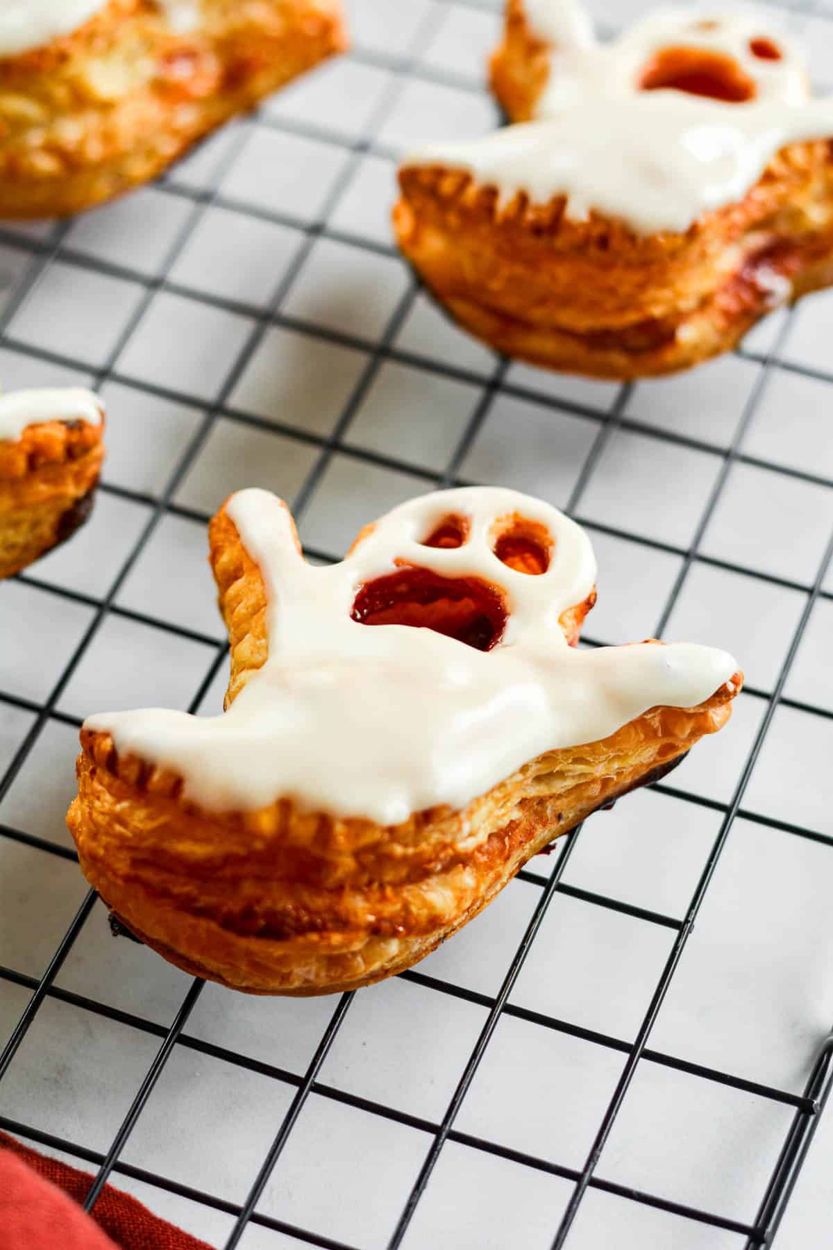 A puffed up ghost-shaped puff pastry topped with white glaze on a wire cooling rack.