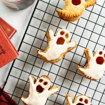 Four glazed ghost puff pastries and one without glaze arranged on a wire cooling rack.