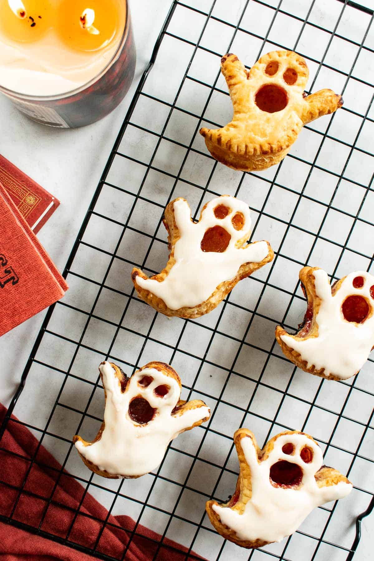 Four glazed ghost puff pastries and one without glaze arranged on a wire cooling rack.