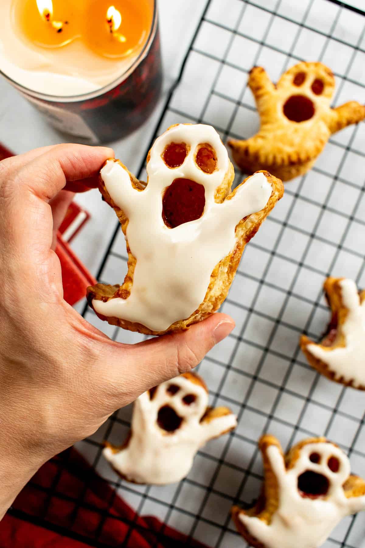 A hand holding a glazed puff pastry in the shape of a ghost with eye and mouth cut-outs.