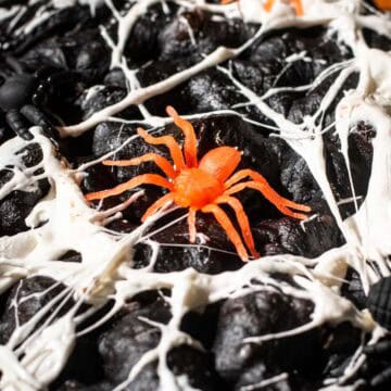 Black focaccia with marshmallows stretched thin across the top with plastic spiders on it.