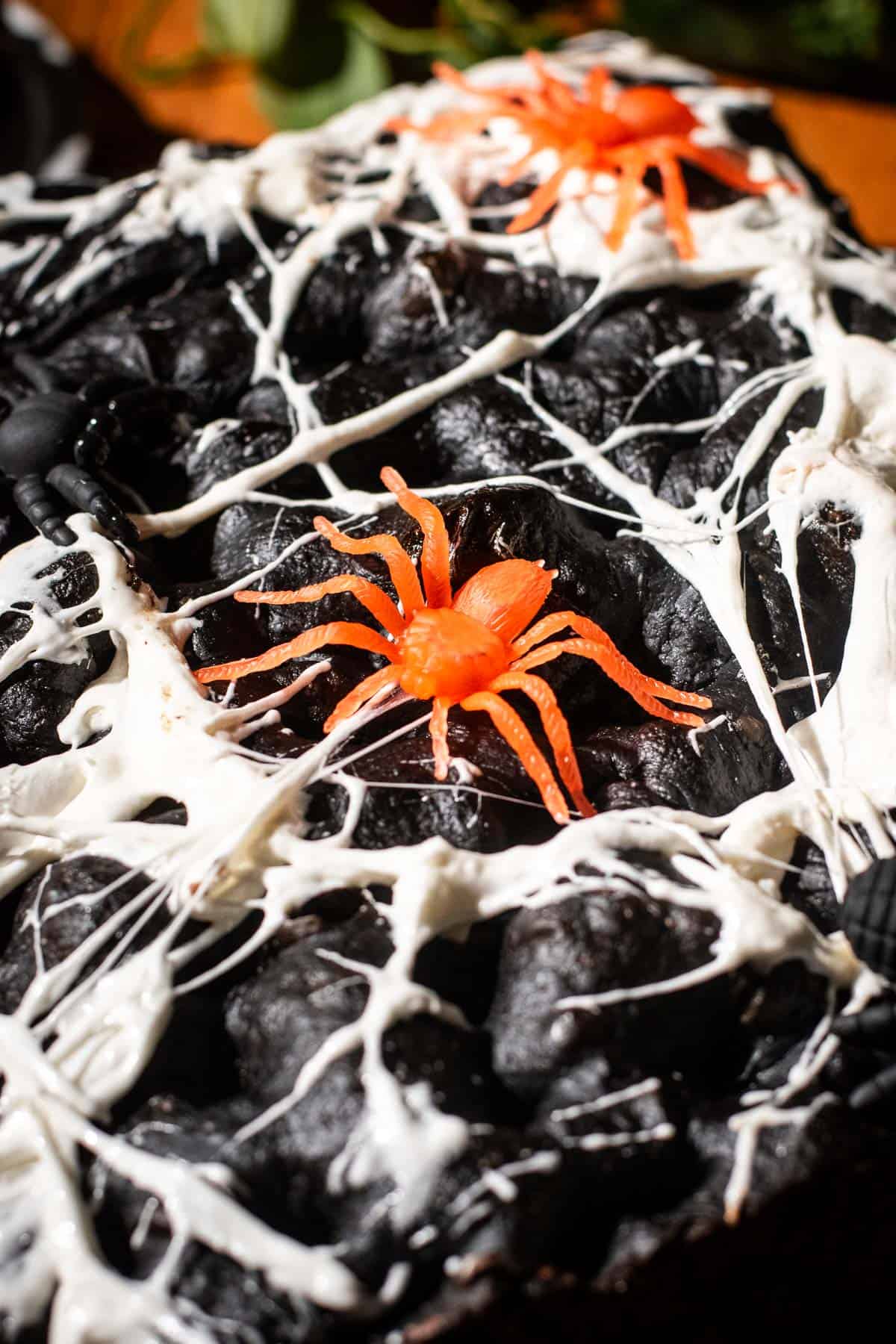 Black focaccia with marshmallows stretched thin across the top with plastic spiders on it.
