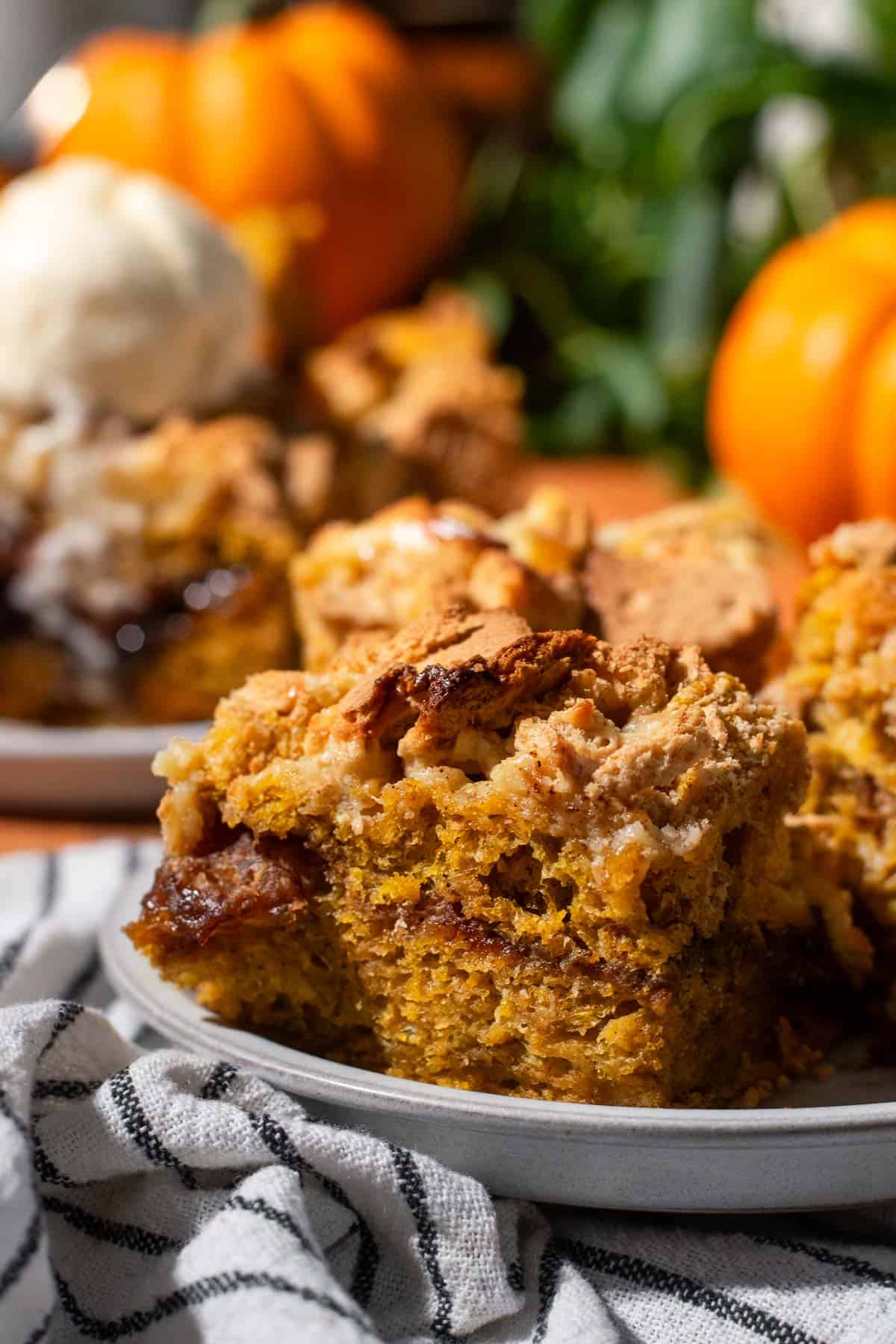A slice of pumpkin focaccia with a brown sugar layer in the middle and crushed graham crackers on top sitting on a grey plate.