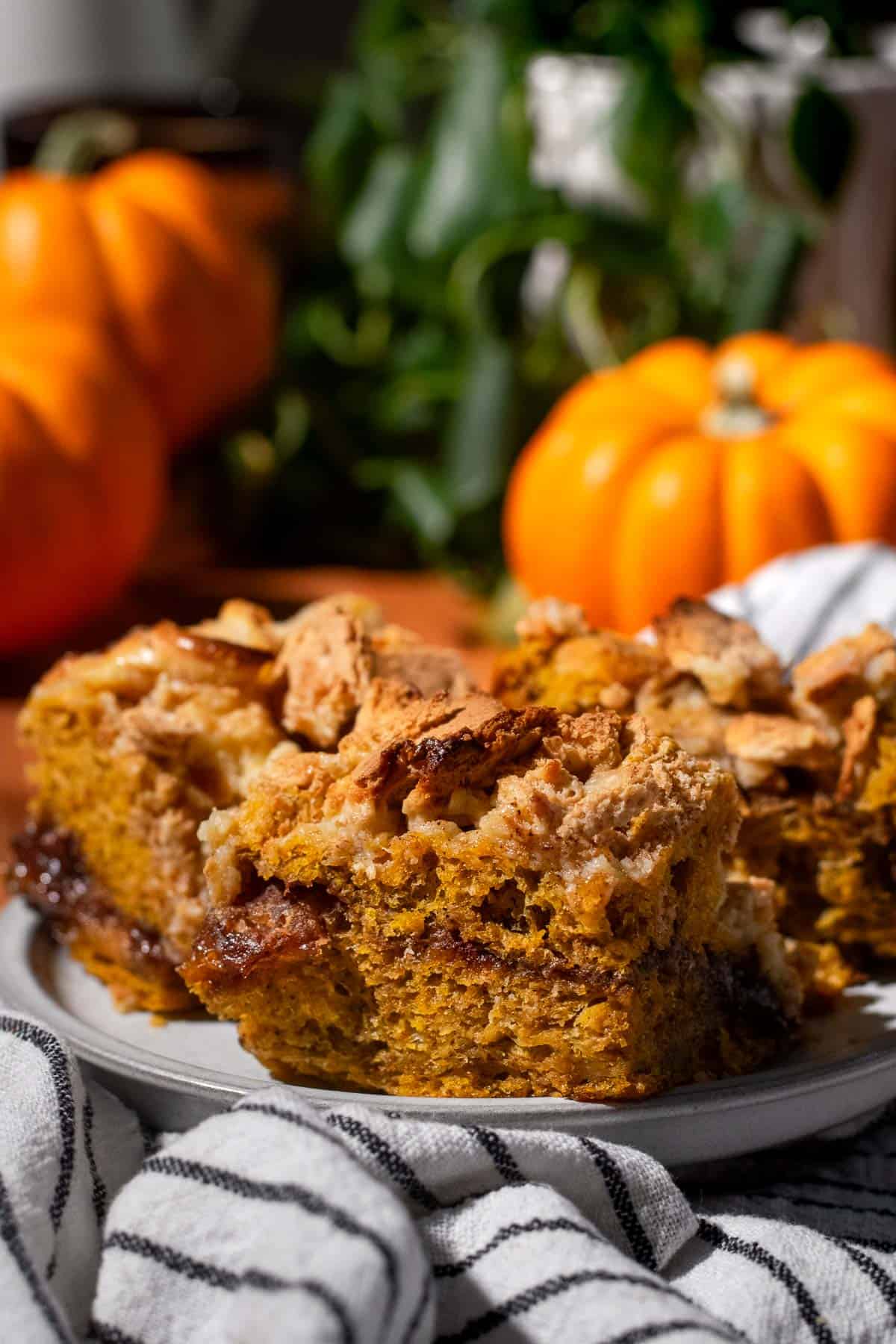 Three pieces of orange pumpkin focaccia topped with cheesecake filling and graham crackers piled on a grey plate.